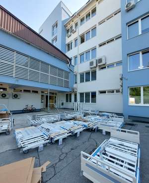 Standing in front of a large white and blue building are several Evario one hospital beds