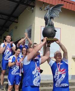 Seven members of the Stiegelmeyer Stolno dragon boat team hold a large trophy in the shape of a dragon into the air and cheer.