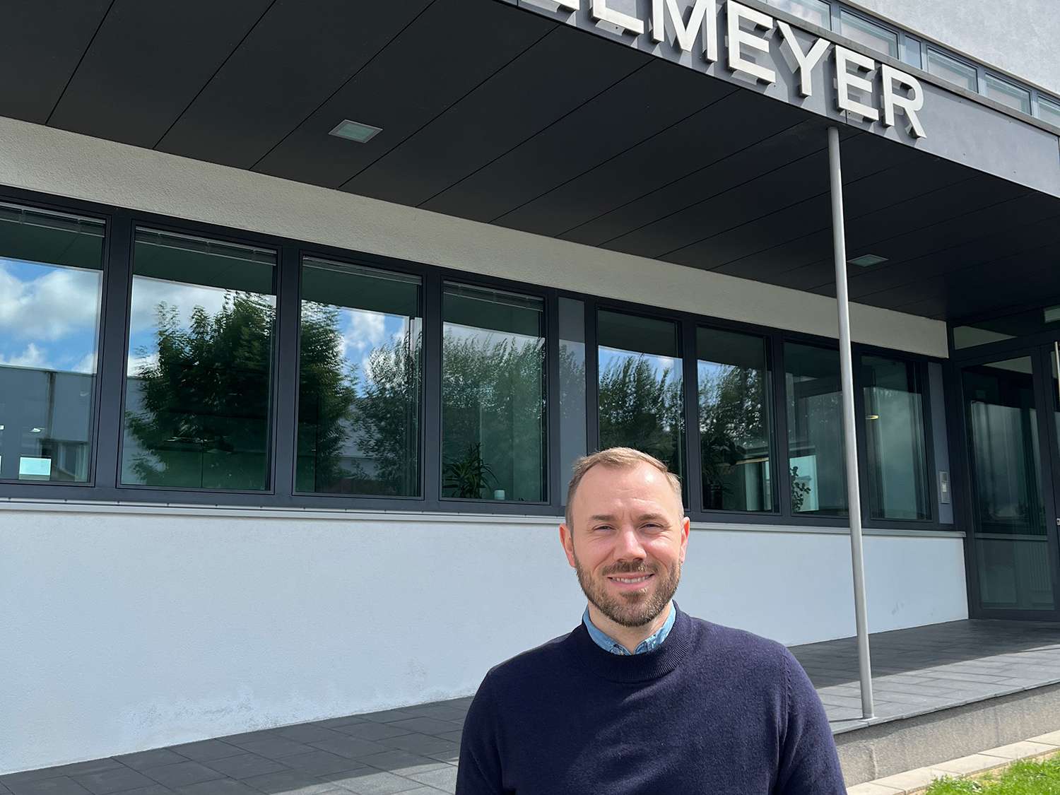 Anton Schlee stands on the pavement in front of the entrance to the Stiegelmeyer administration building in Herford and smiles into the camera.