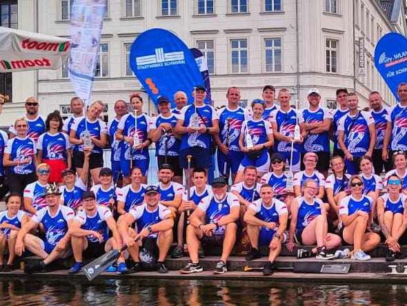The large dragon boat team from Stiegelmeyer Stolno sits and stands in front of a building in Schwerin and smiles into the camera.